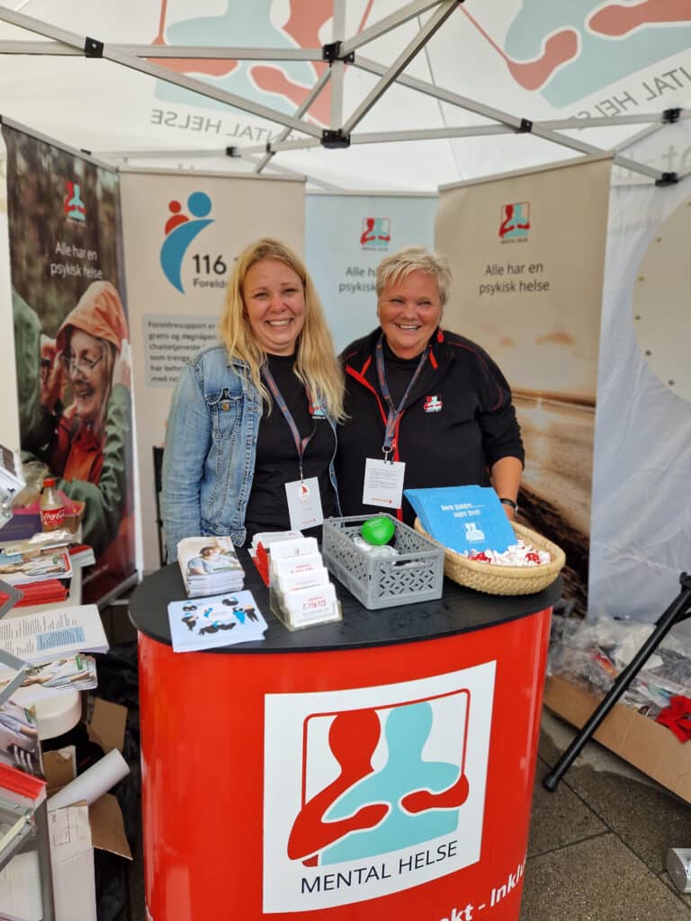 Bilde av to blide kvinner fra Mental Helse på stand på Arendalsuka 2022.
