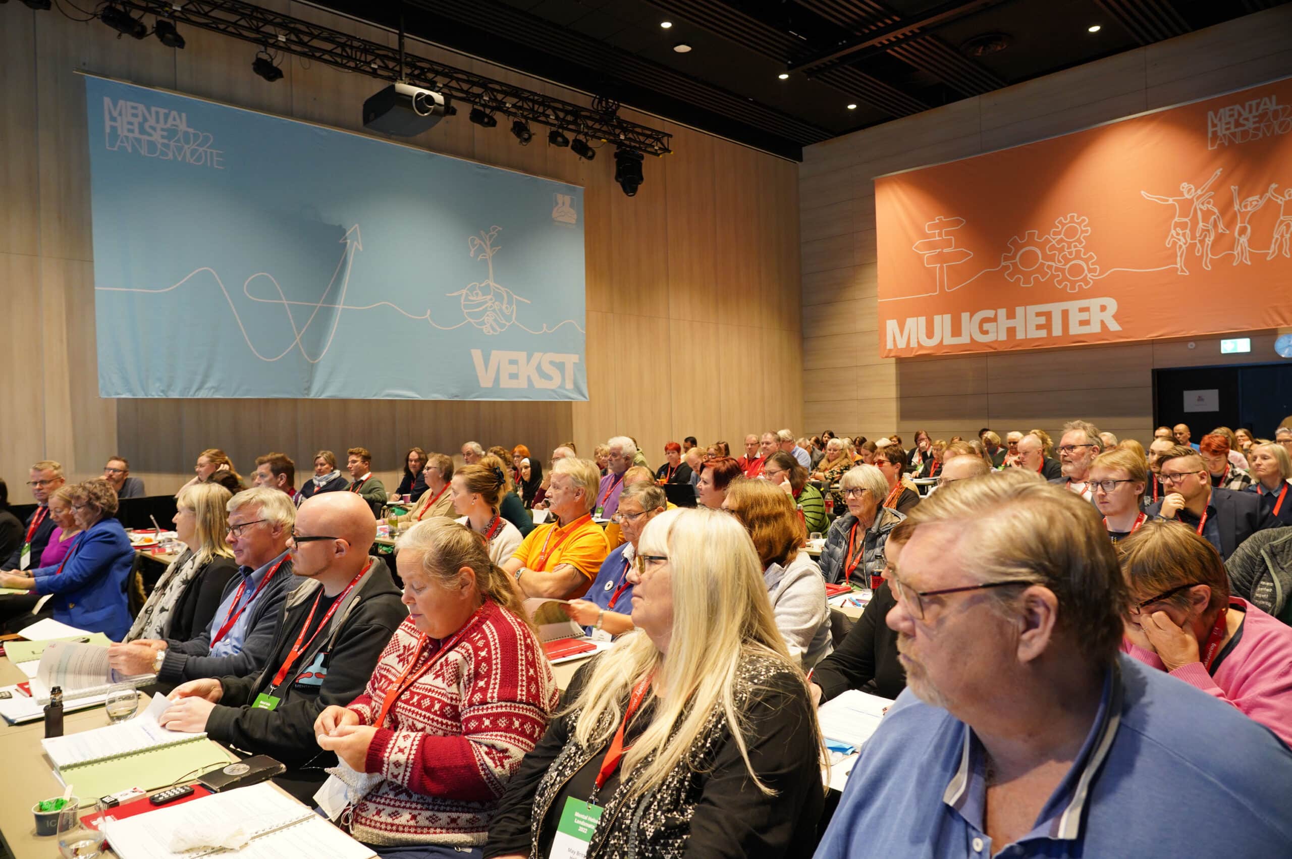 Mange mennesker sitter og følger med på noe i et konferanserom. Bilde av salen på Mental Helses landsmøte 2022.