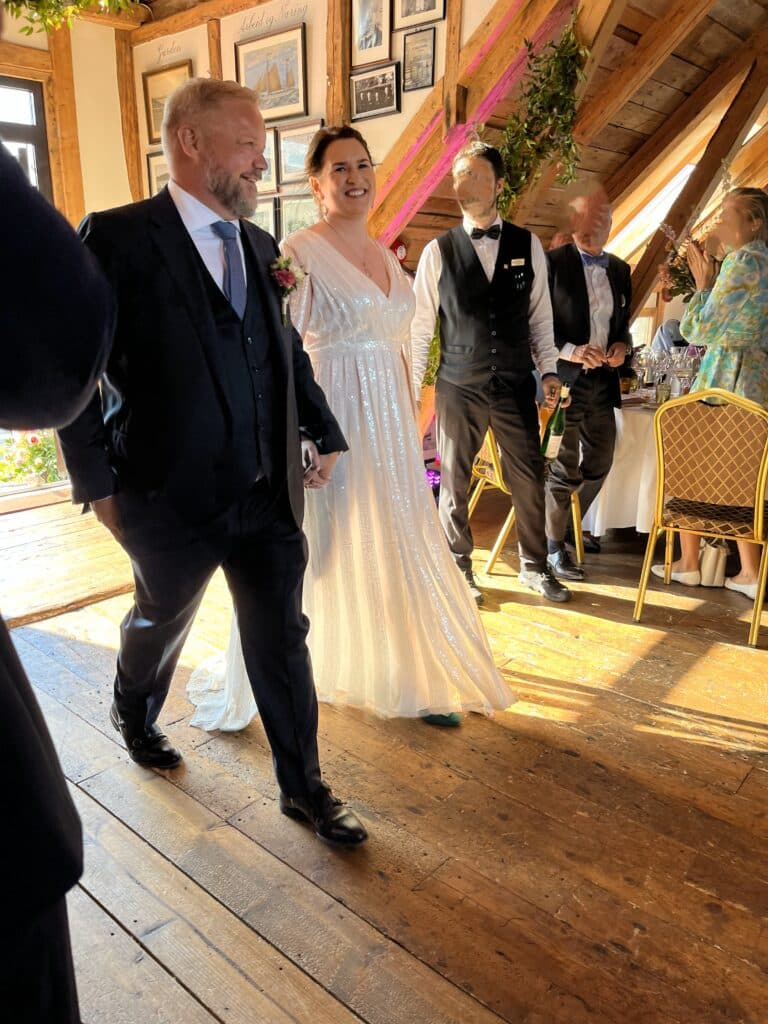Et par i dress og brudekjole holder hender og smiler.