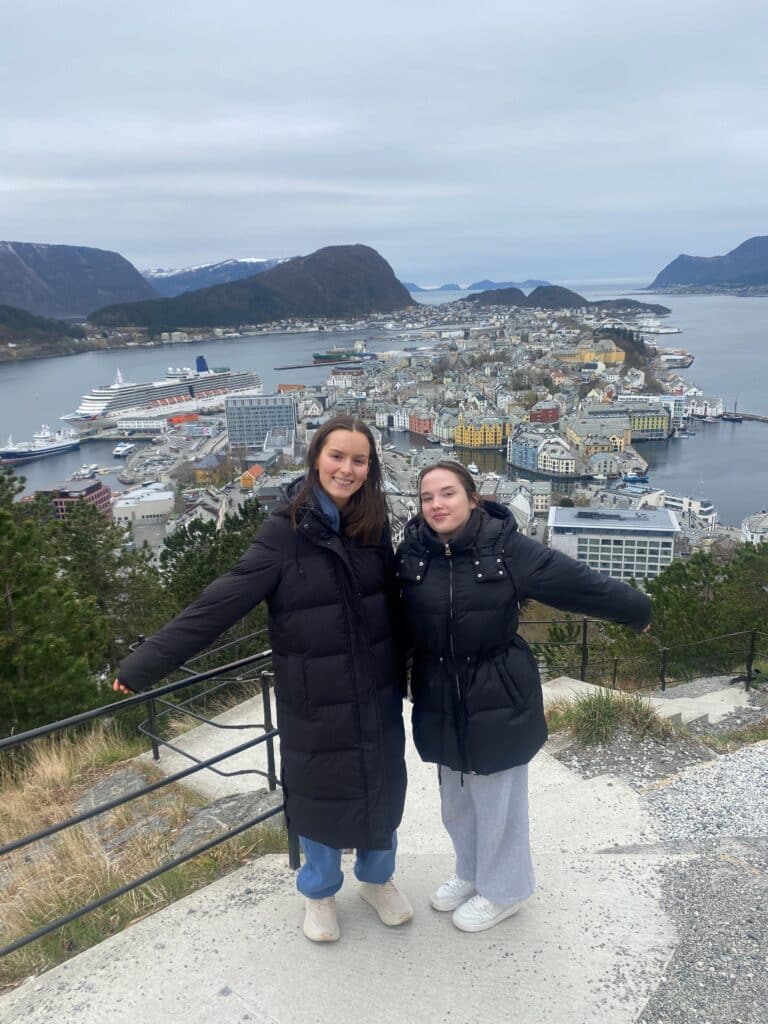 To jenter står foran ett rekkverk med utsikt til by.