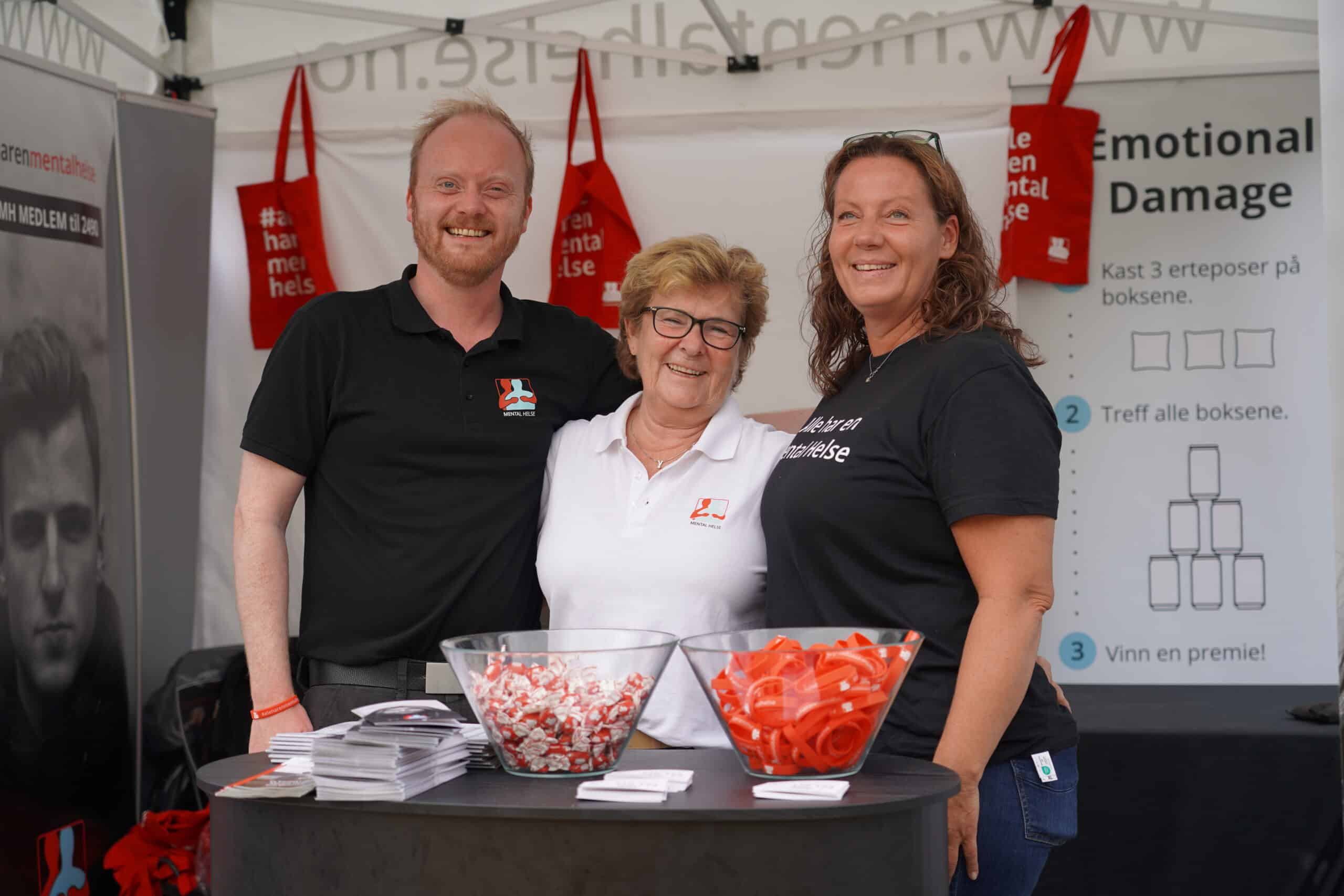 Tre mennesker smiler mens de står på stand.