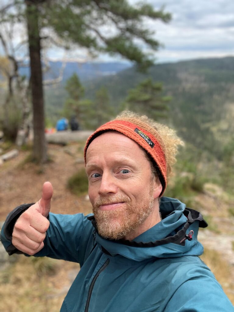 Trygve smiler og gir tommel opp med naturen som bakgrunn