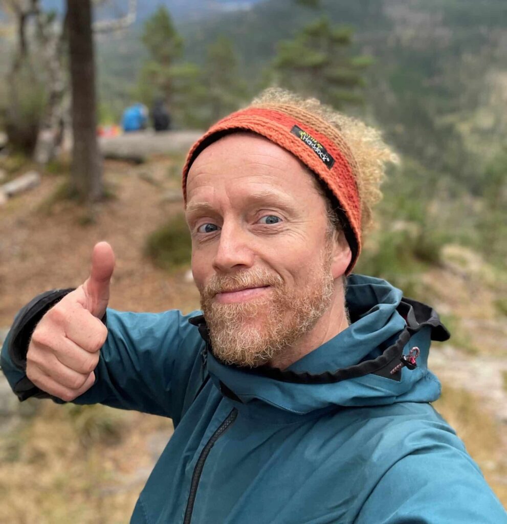 Trygve smiler og gir tommel opp med naturen som bakgrunn
