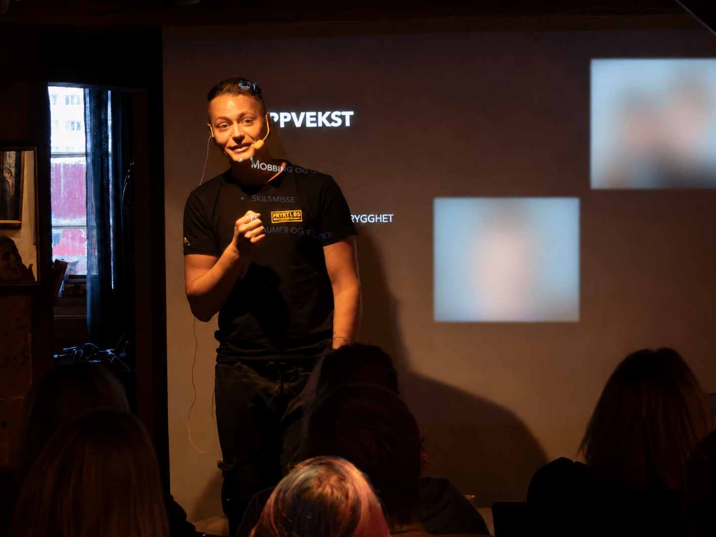 Aleksander Martinsen holder foredrag foran publikum på Wirumbrygga i Kristiansund. To bildefelt på lerretet bak ham er sladdet.